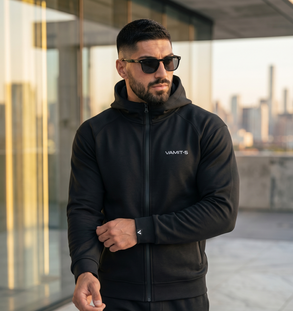 Man wearing a black tracksuit with 'VAMIT-5' branding outdoors.


